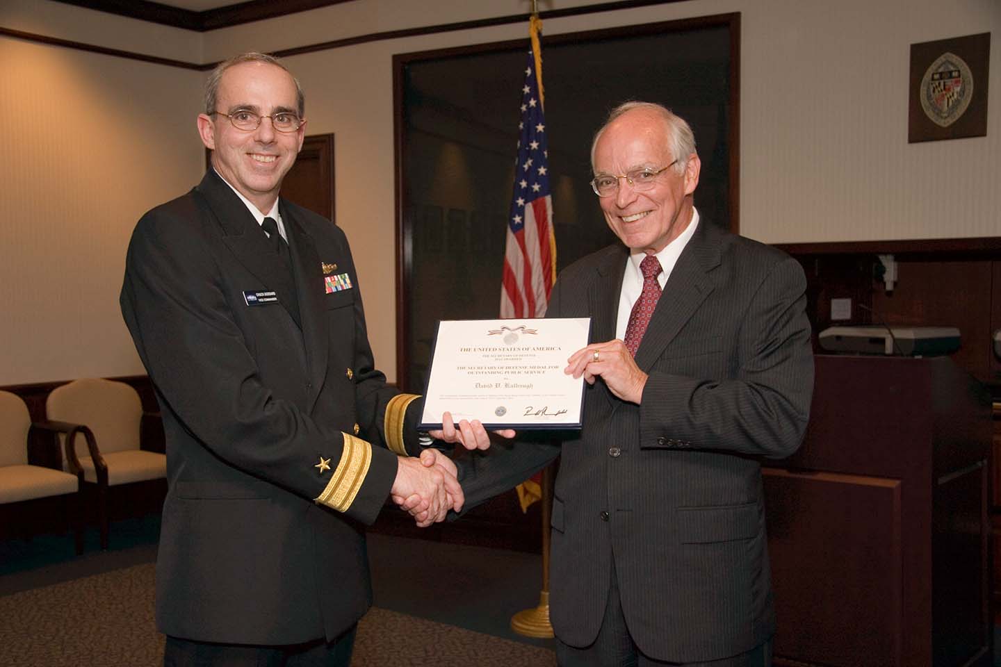 Rear Admiral "Chuck" Goddard presents the certificate for the Secretary of Defense Medal to Dave Kalbaugh