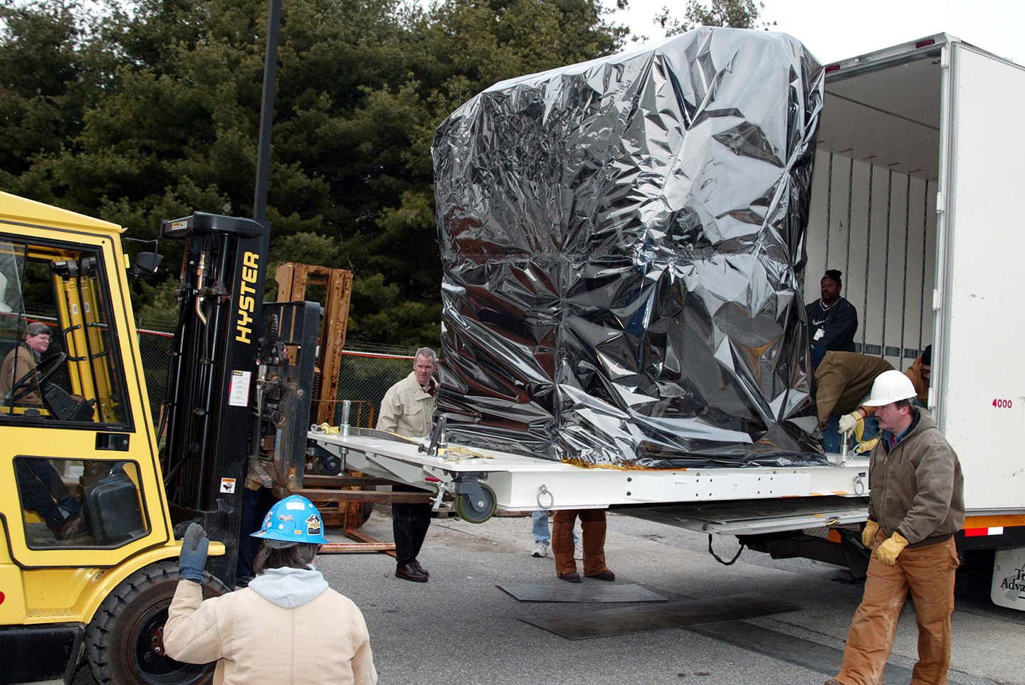 Wrapped in a “double bag“ of protective Llumalloy film, the MESSENGER spacecraft is loaded into a moving van
