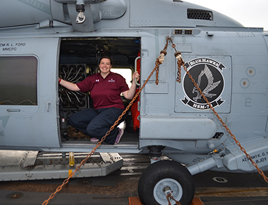 Heather James poses with an MH-60 helicopter during her Scientists to Sea excursion aboard the USS Mobile Bay (CG-53) at sea.