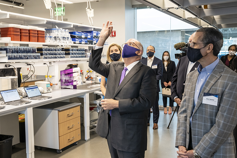 Maryland Gov. Larry Hogan (center) examines a small chip capable of performing genomic sequencing as APL Board of Managers Chair Heather Murren and Director Ralph Semmel look on.