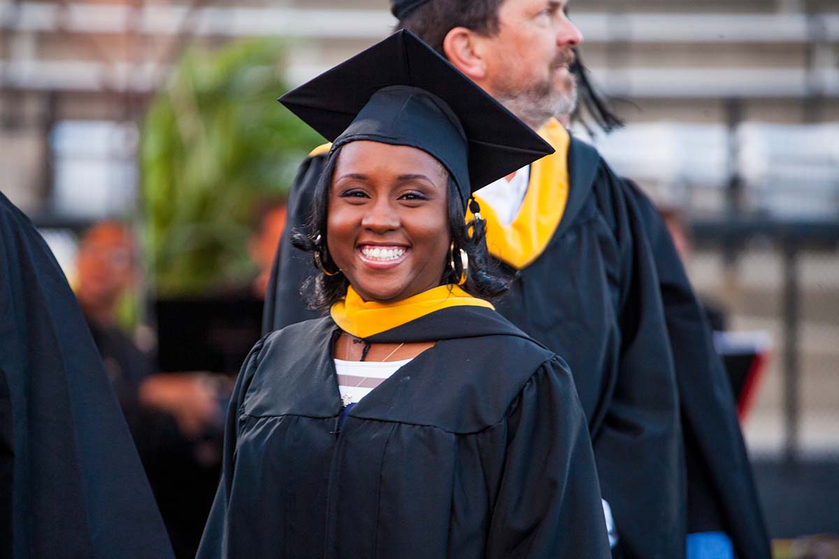 A Johns Hopkins Engineering for Professionals student wearing graduation robes smiles at the camera.