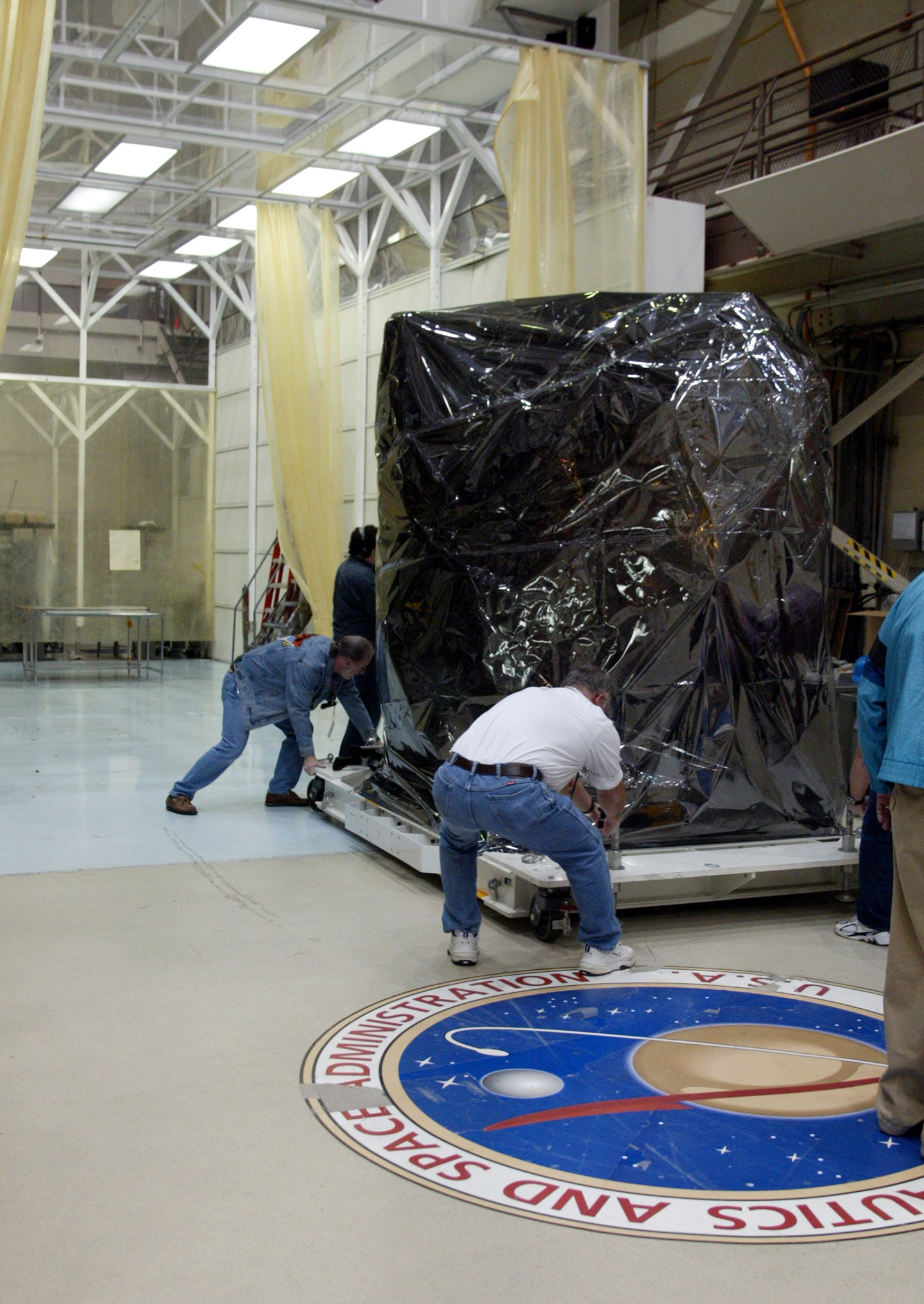 Team members move the MESSENGER spacecraft, wrapped in protective film, out of its temporary clean room