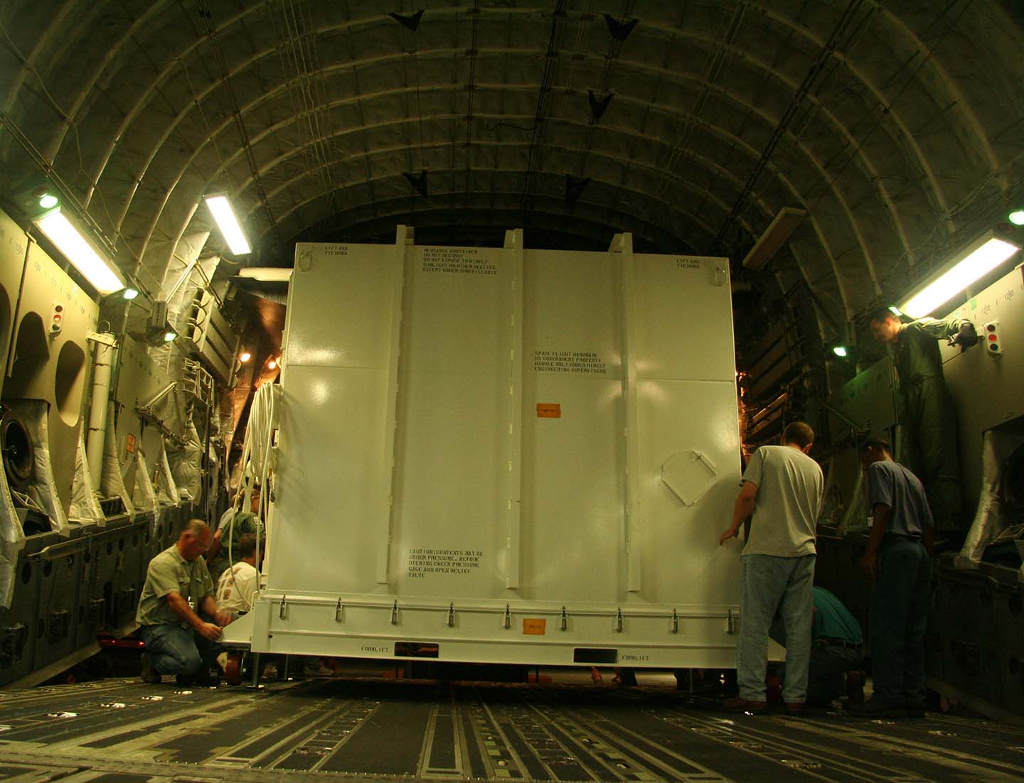 Mission team members and ground crew prepare to unload the shipping "can" containing the New Horizons spacecraft