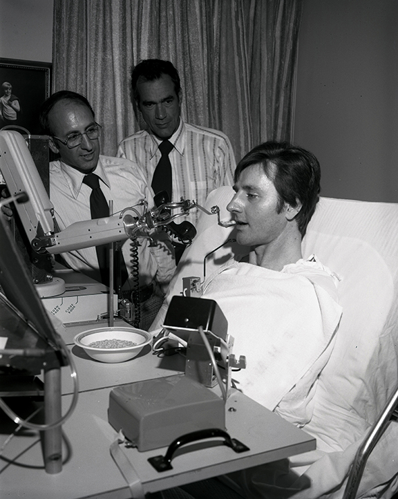 A robotic arm—commanded by a chin-movement controller—allows patient John Craven to perform tasks, including reading and feeding himself