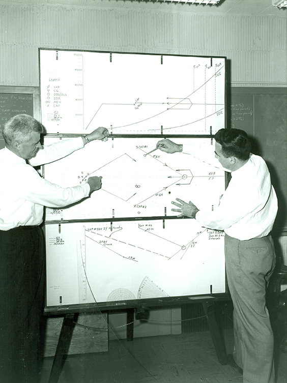 Stuart Ball (left) and John Long use Air Battle Analyzer nomographs to correlate horizontal, vertical, and time perspectives of a tactical situation. (1959)