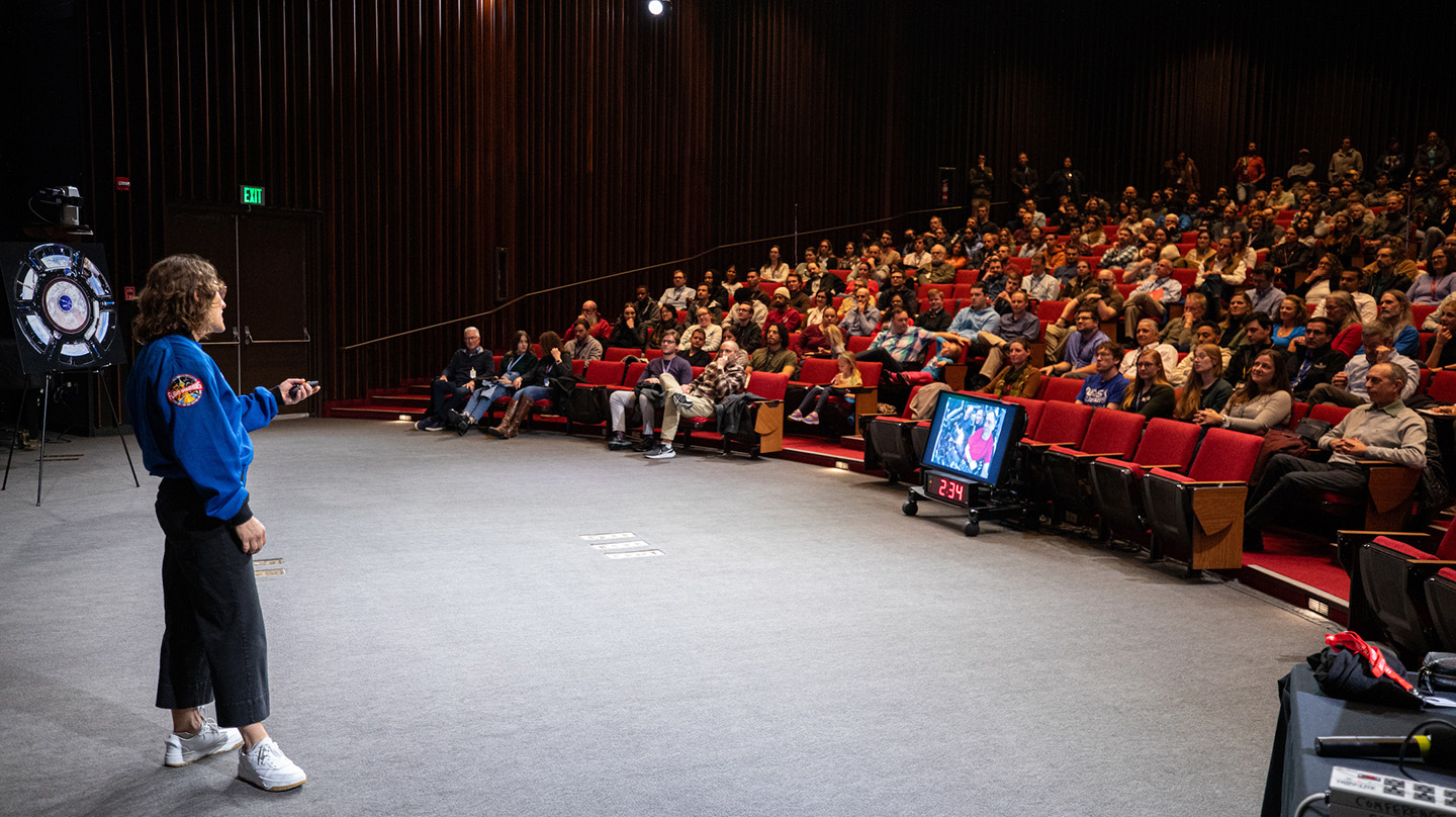 Christina Koch speaks in front of a full audience in APL's Kossiakoff Center