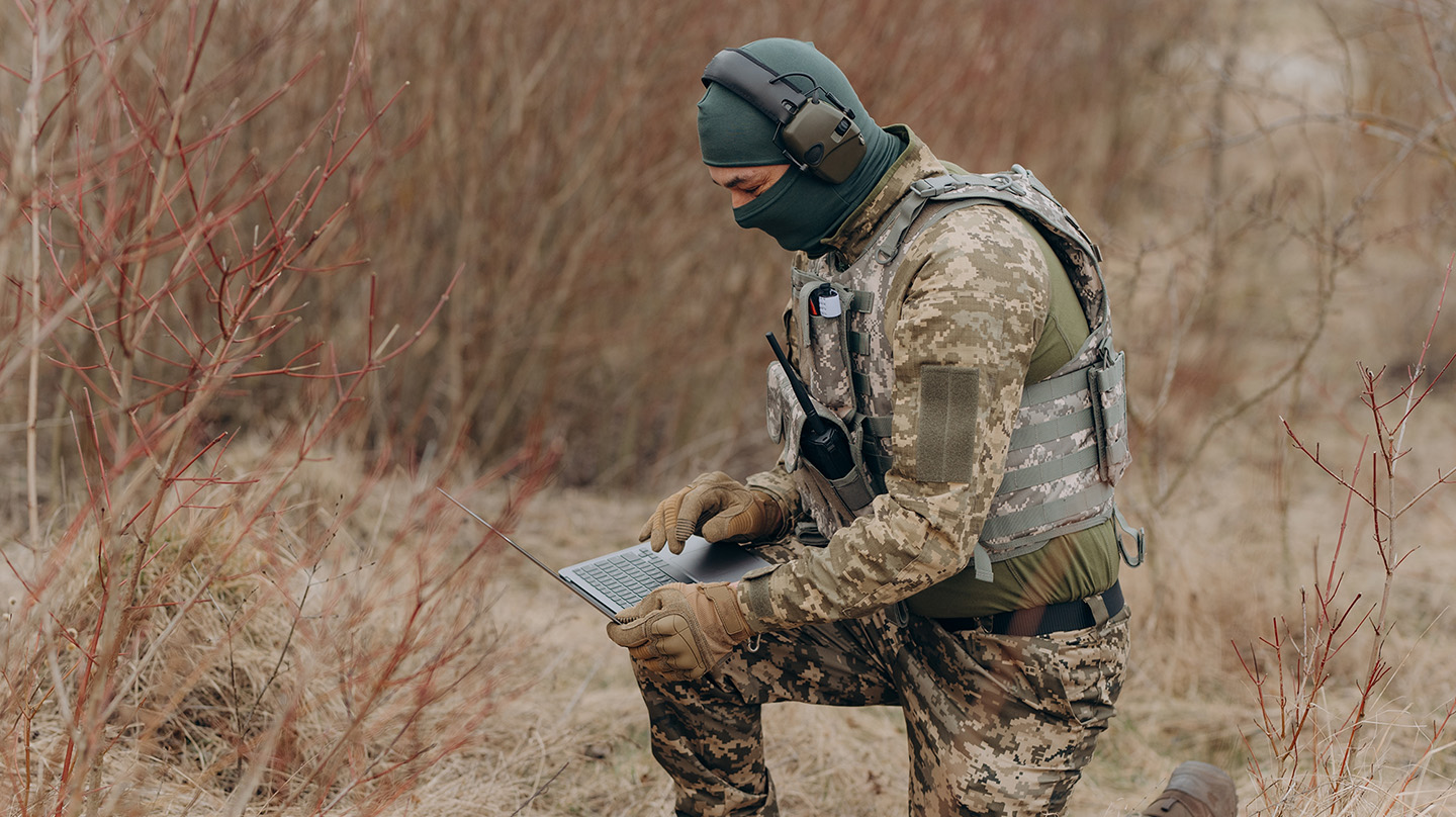 A solider in a forest reviews information on a laptop