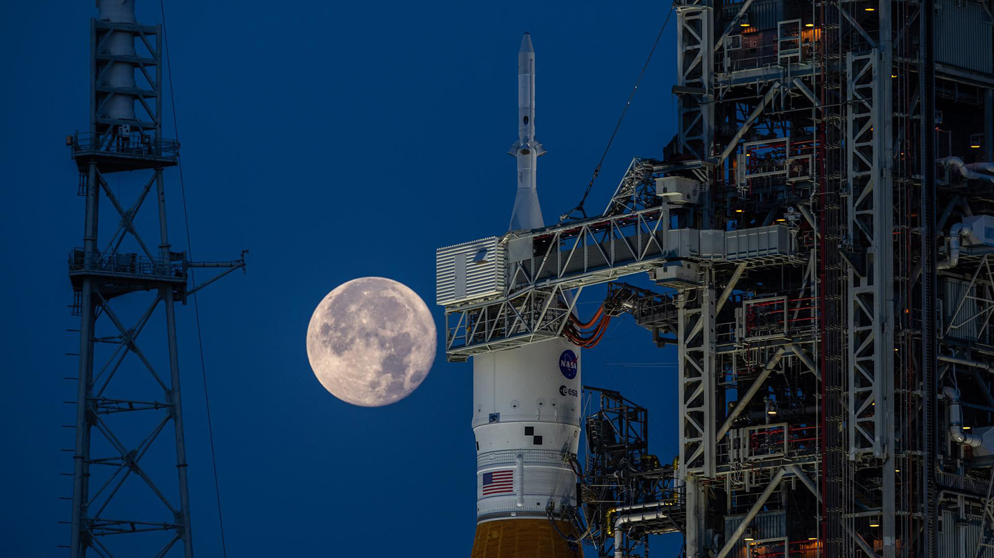 A full moon hangs in the sky behind a shuttle